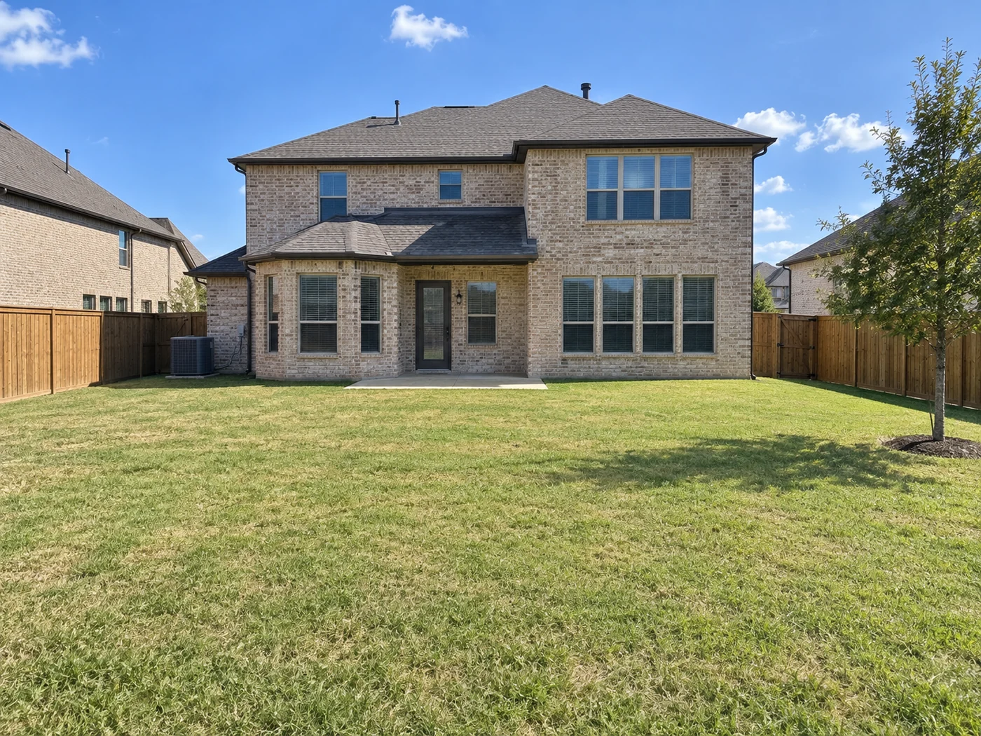 A plain grass backyard behind a two-story Dallas-Fort Worth brick home before work began
