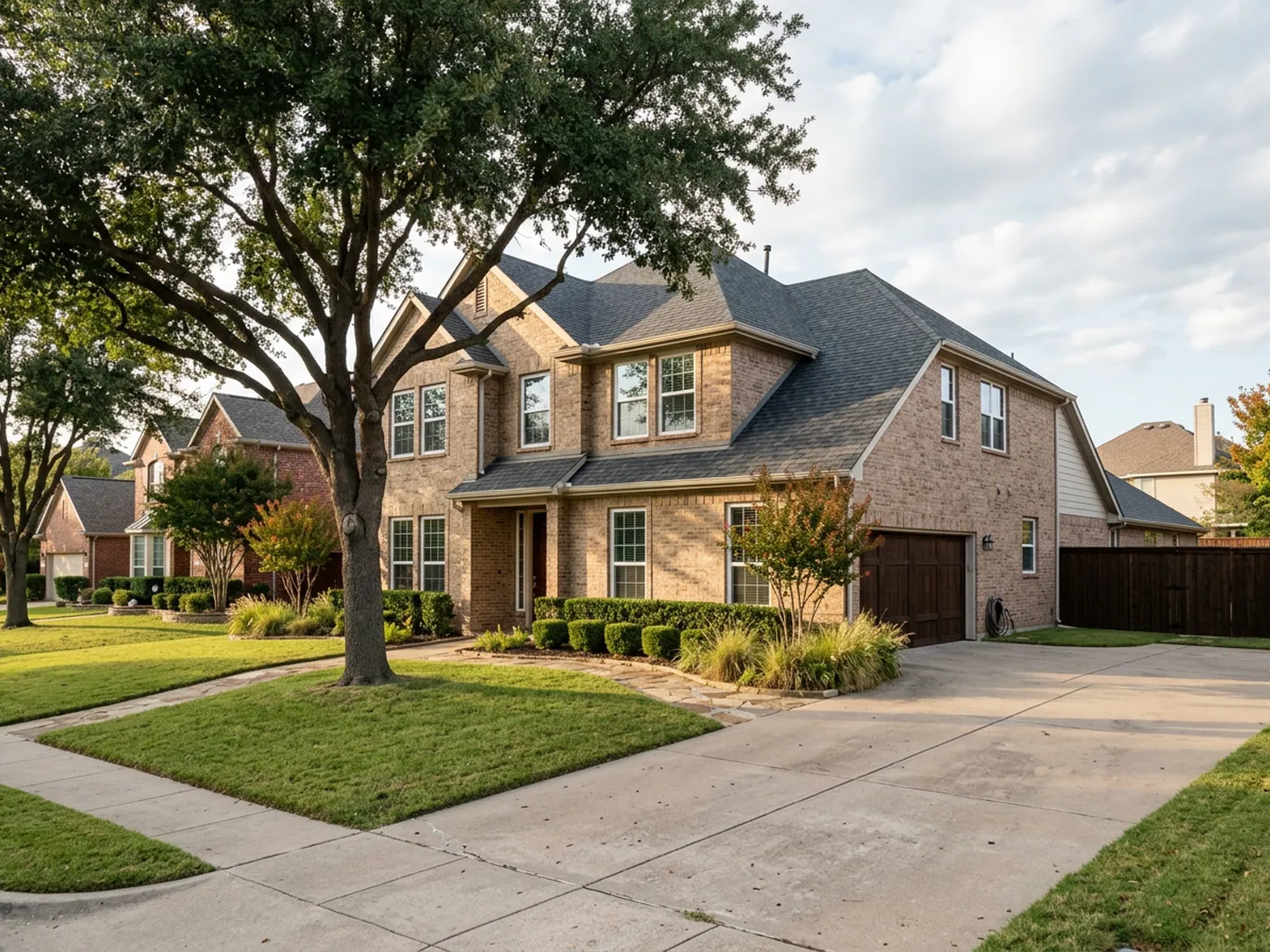 Two-story tan brick North Texas home with white-framed double-hung windows on the west elevation in late afternoon sun