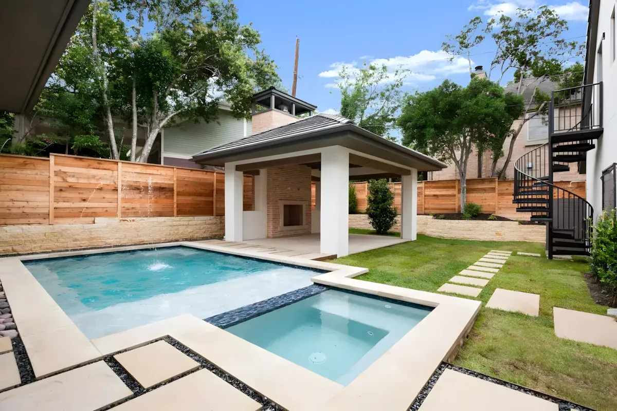 Rectangular pool and raised spa beside a covered cabana in a fenced backyard