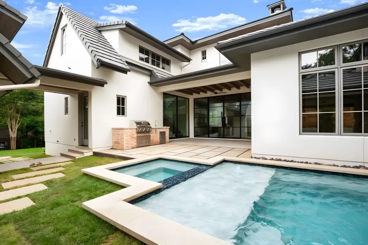 Pool and spa wrapping a modern white farmhouse with a built-in grill station
