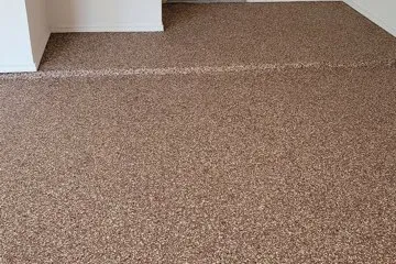 Brown speckled epoxy coated floor extending across a garage and raised step beside white walls