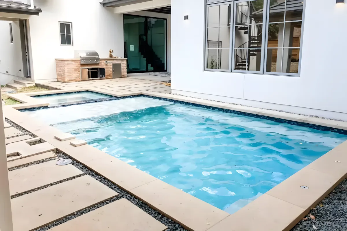 Pool and sun deck behind a white home with a standing-seam roof