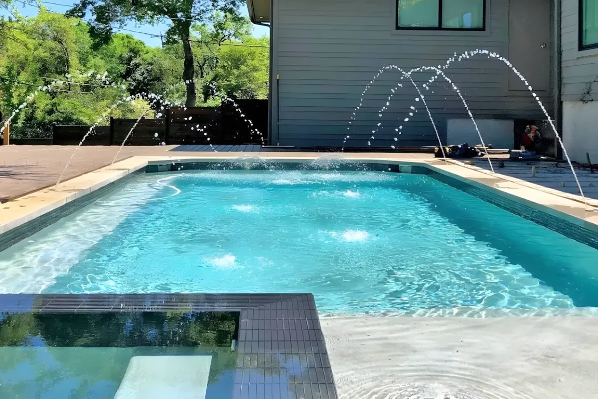 Deck jets arcing over a pool beside a modern home