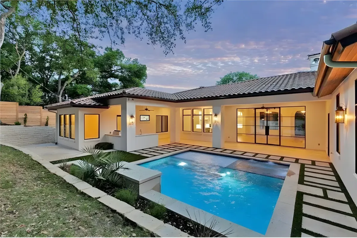 Pool lit at twilight in front of a warmly lit ranch home