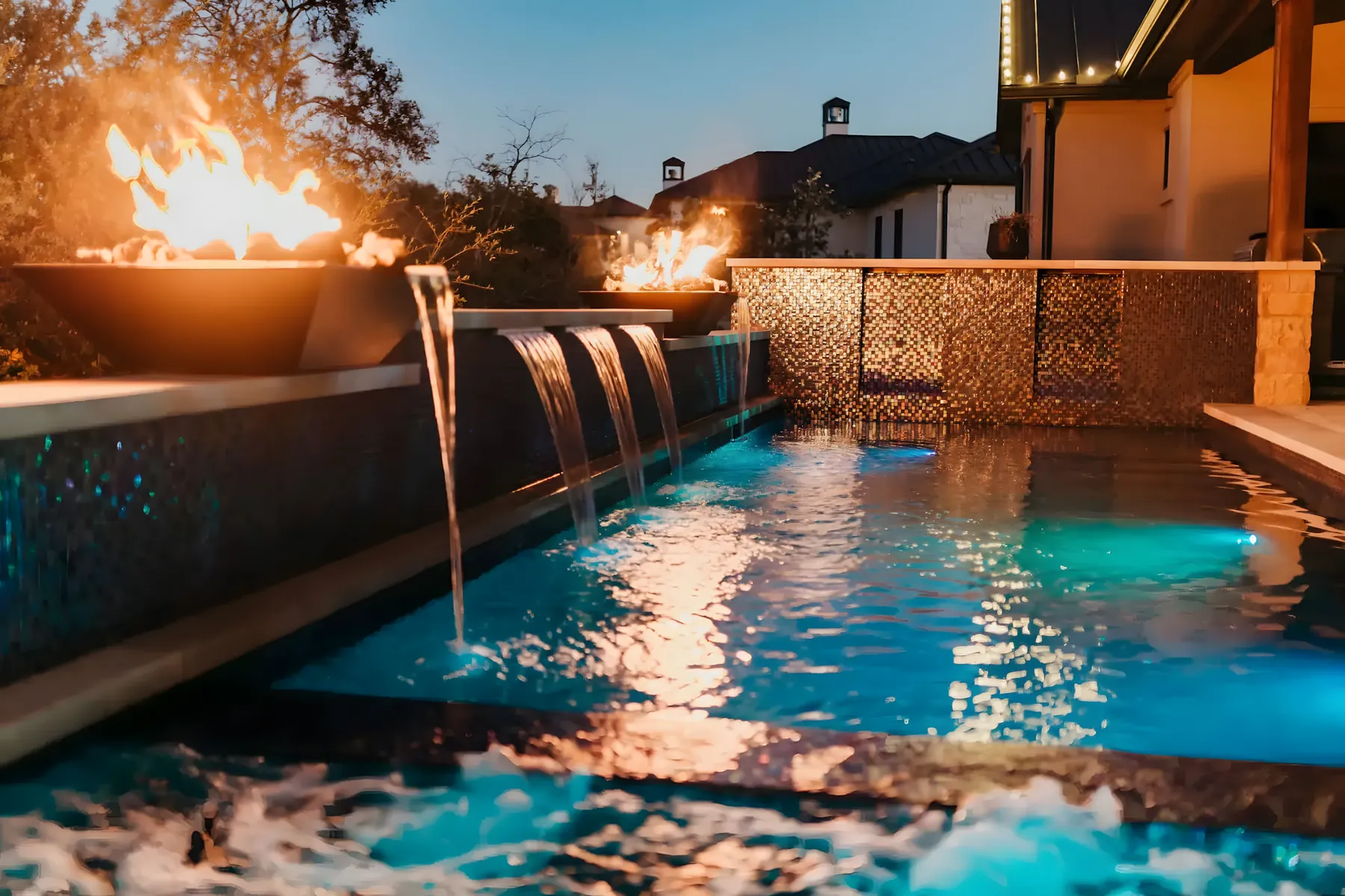 Fire bowls and sheer-descent waterfalls spilling into a lit pool at night