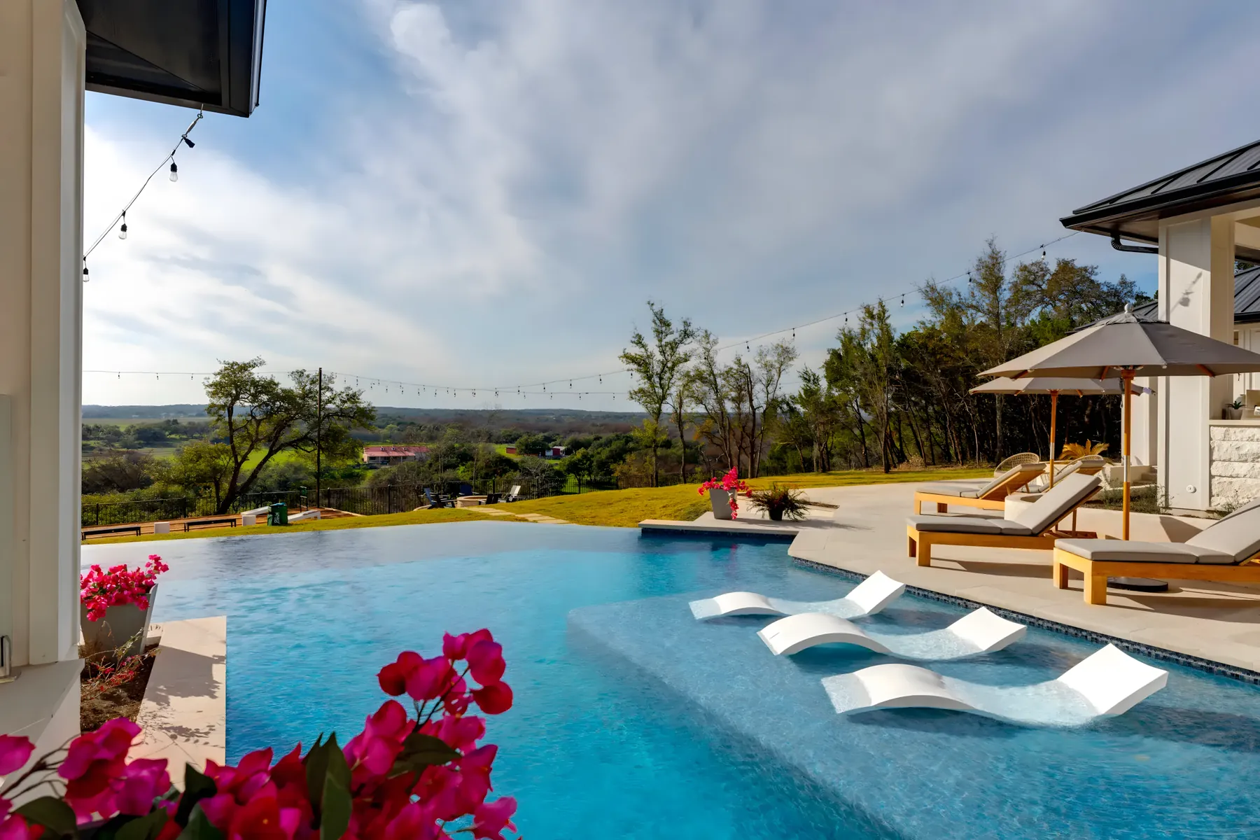 Infinity-edge pool with in-water loungers above a wooded North Texas valley