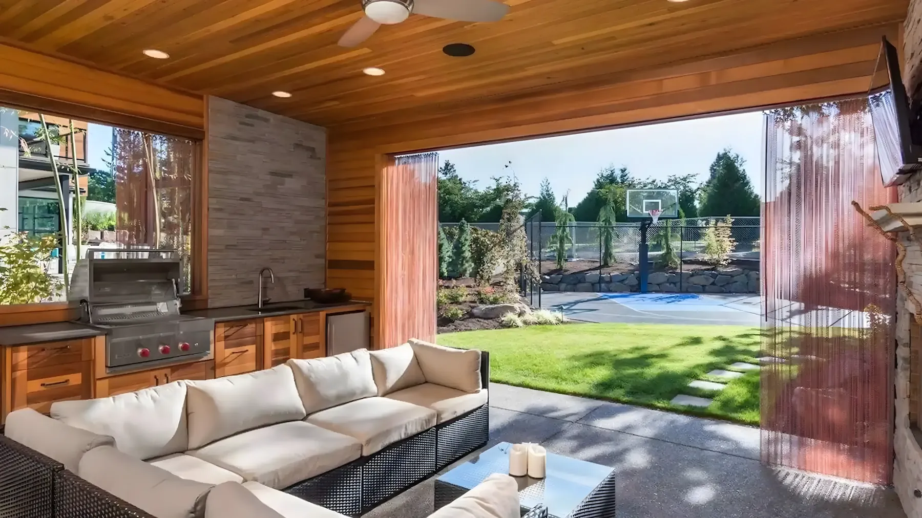 Covered outdoor living room with a sectional, built-in grill and cedar ceiling