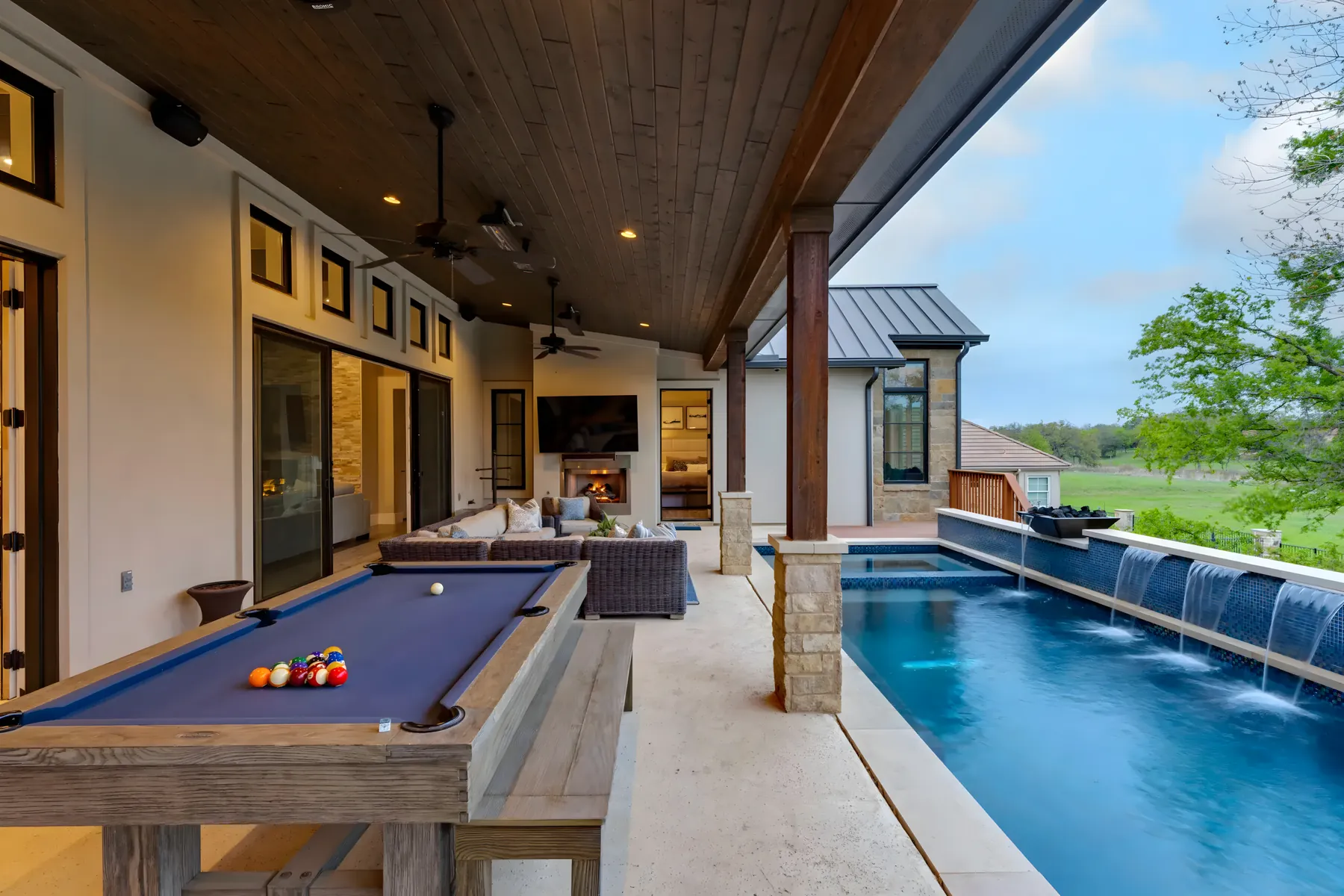 Covered patio with a pool table beside a long lap pool