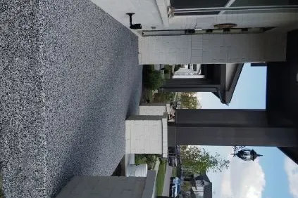 Speckled gray coated patio beside a white house, with covered entry and landscaped yard
