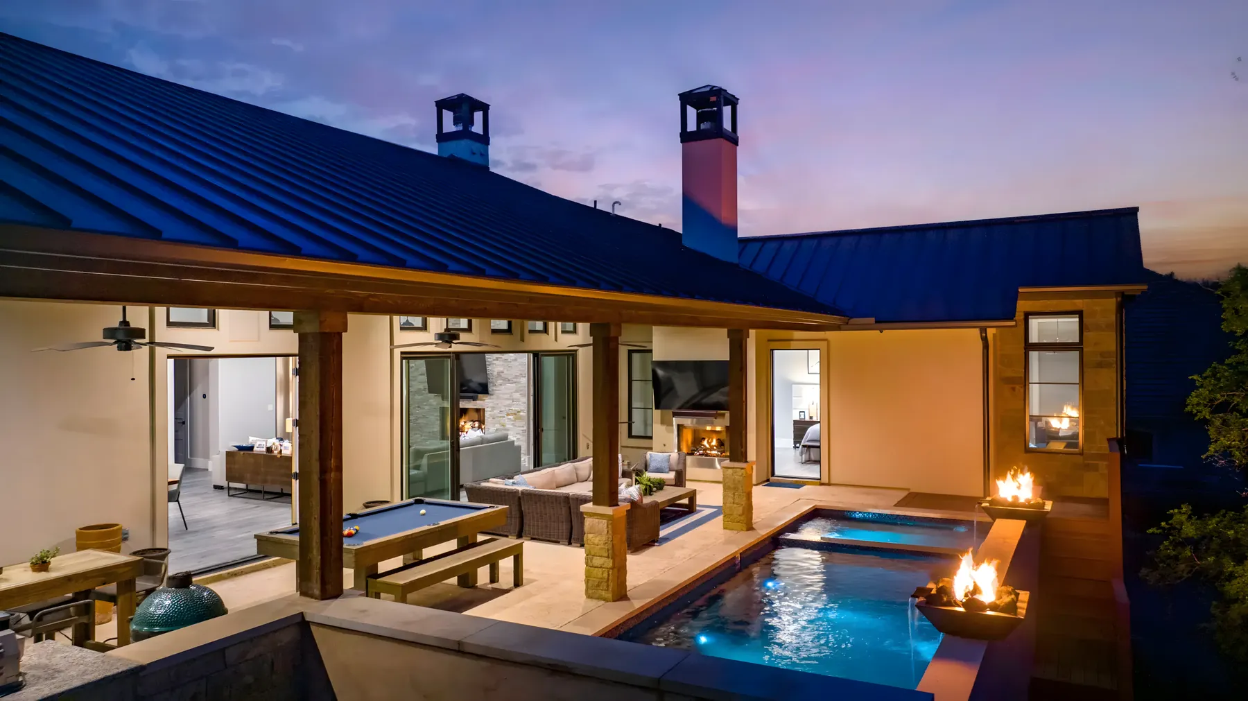 Covered patio with a fire feature and spa glowing at twilight