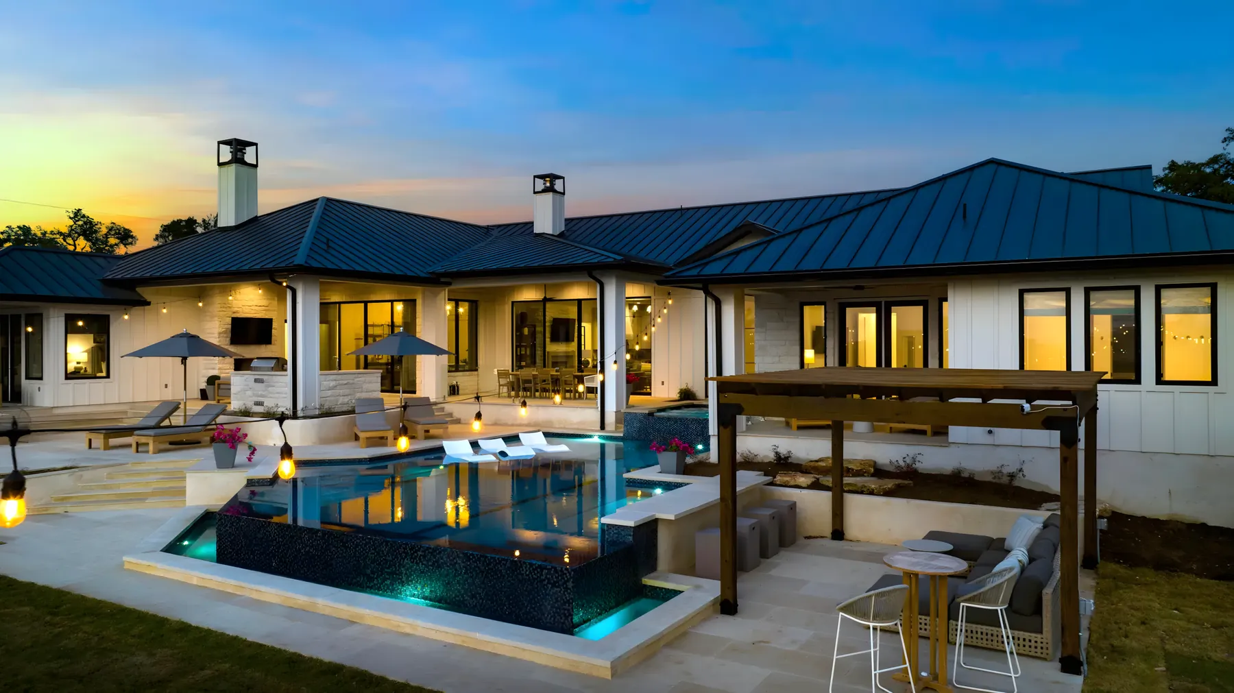 Aerial view of a lit pool, pergola and covered patio at dusk