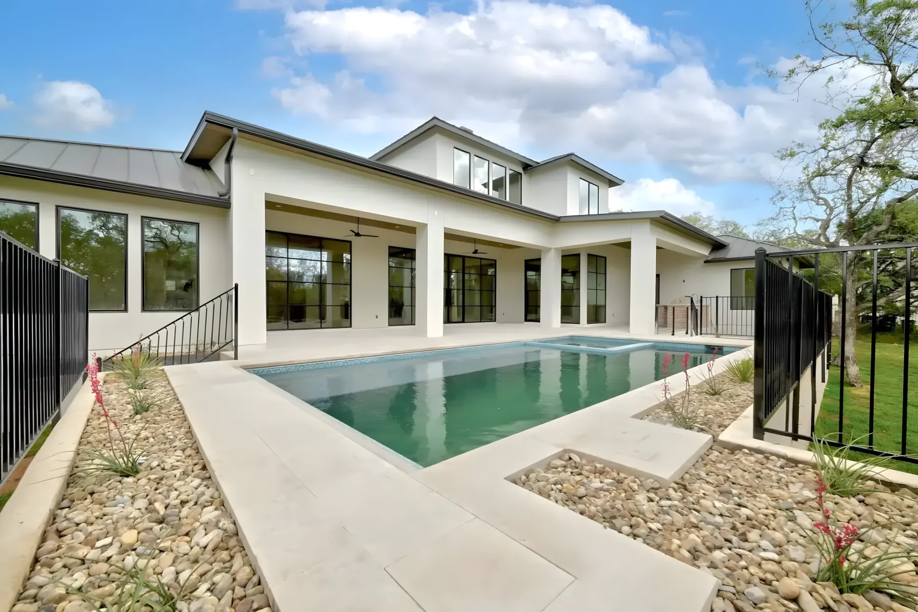 Rectangular pool and limestone deck behind a white modern home