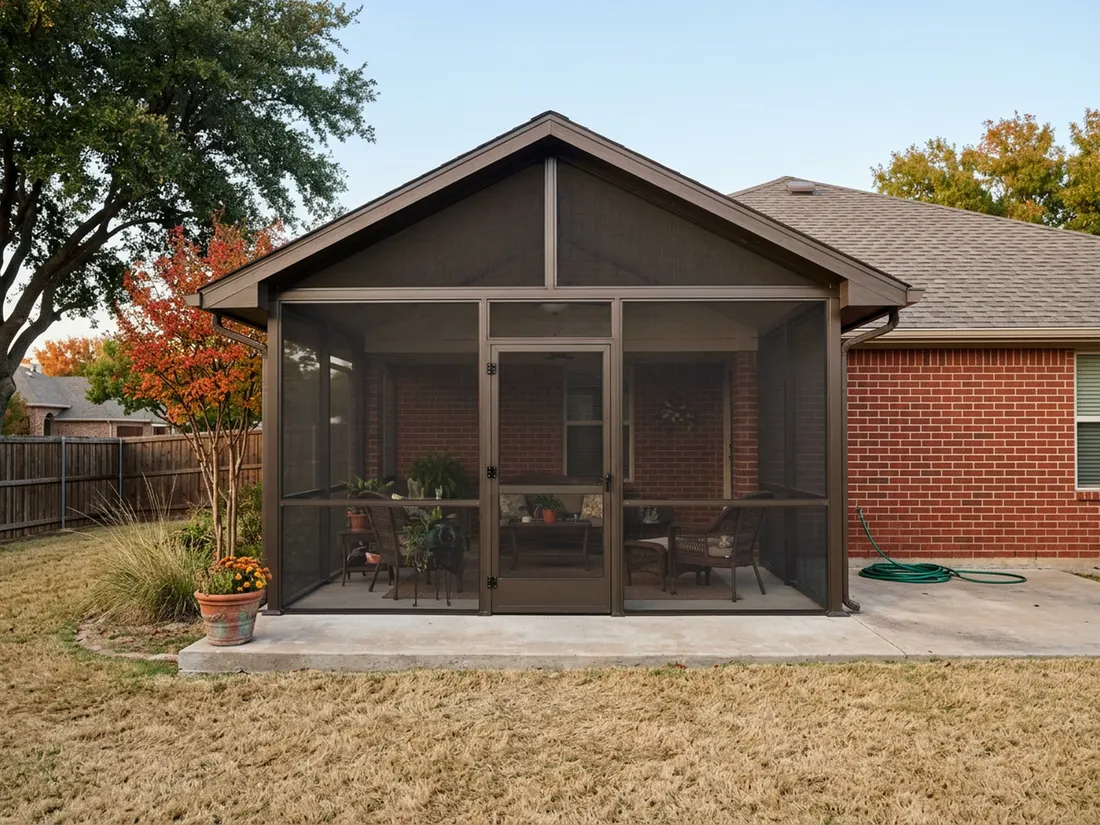Finished bronze-framed screened patio enclosure on a red-brick North Texas home in warm autumn afternoon light