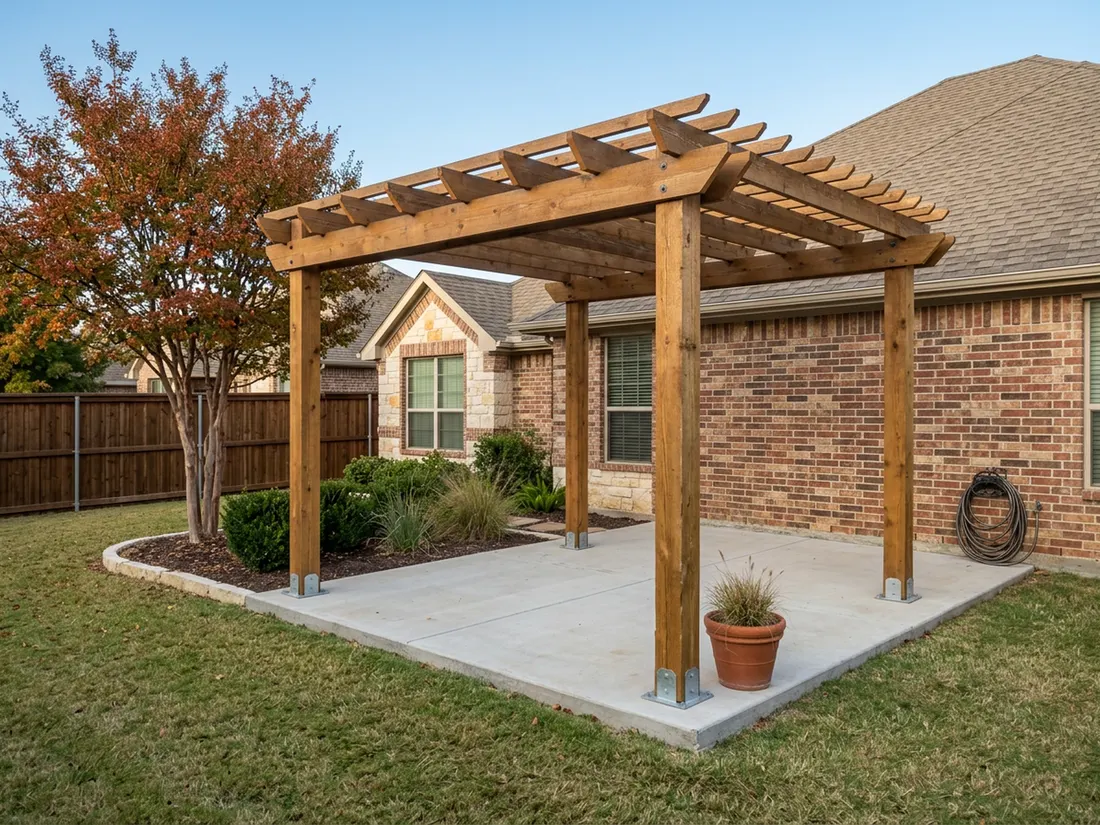 Wide view of a stained cedar pergola on standoff post bases beside a North Texas brick home in fall