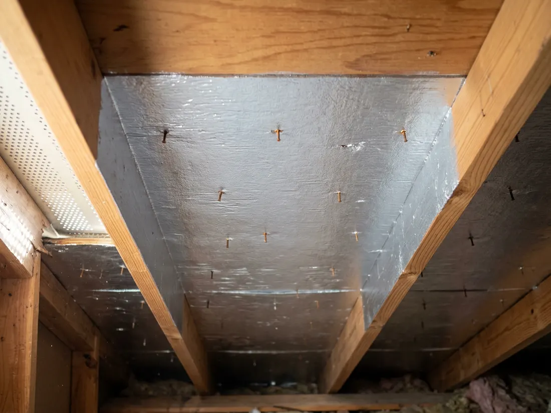 Close view of silver liquid foil coating on the underside of roof decking between wooden rafters in a Texas attic