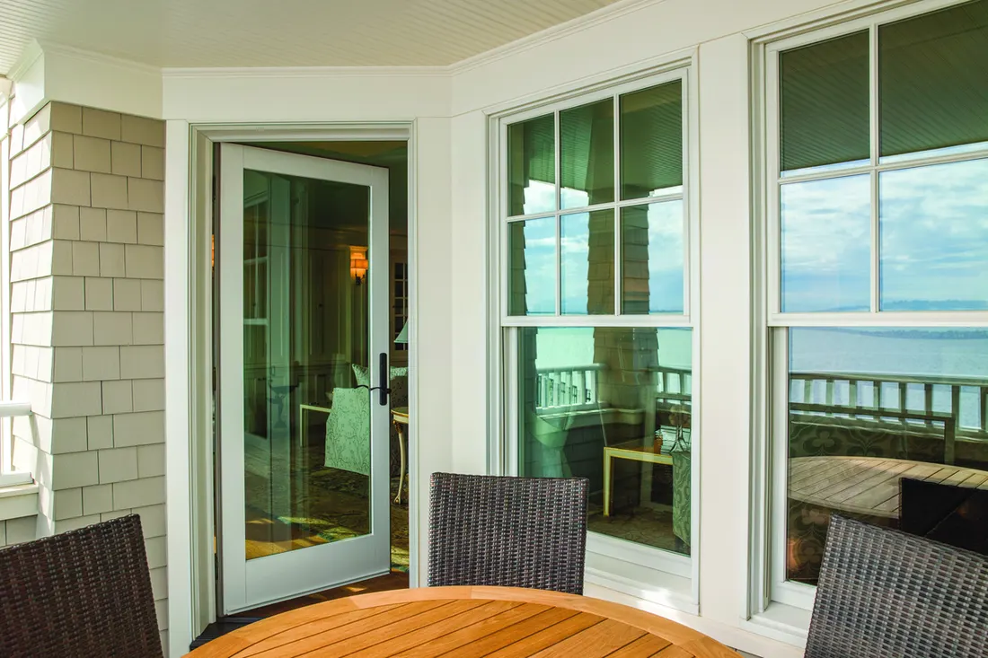 Large white double-hung windows and a glass patio door along a covered porch with siding