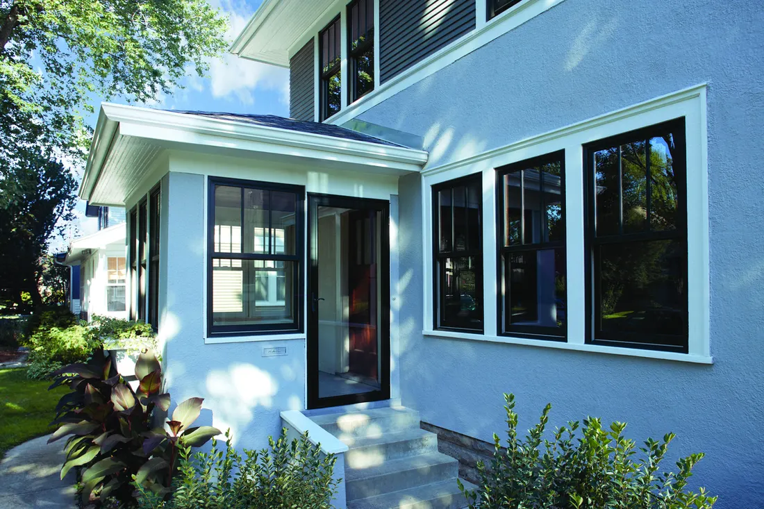 Black framed windows with white trim on a light blue stucco house exterior