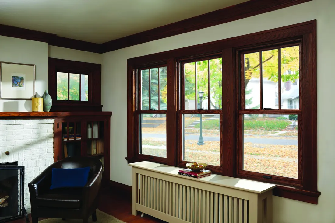 Three dark wood-framed double-hung windows installed in a living room above a radiator cover