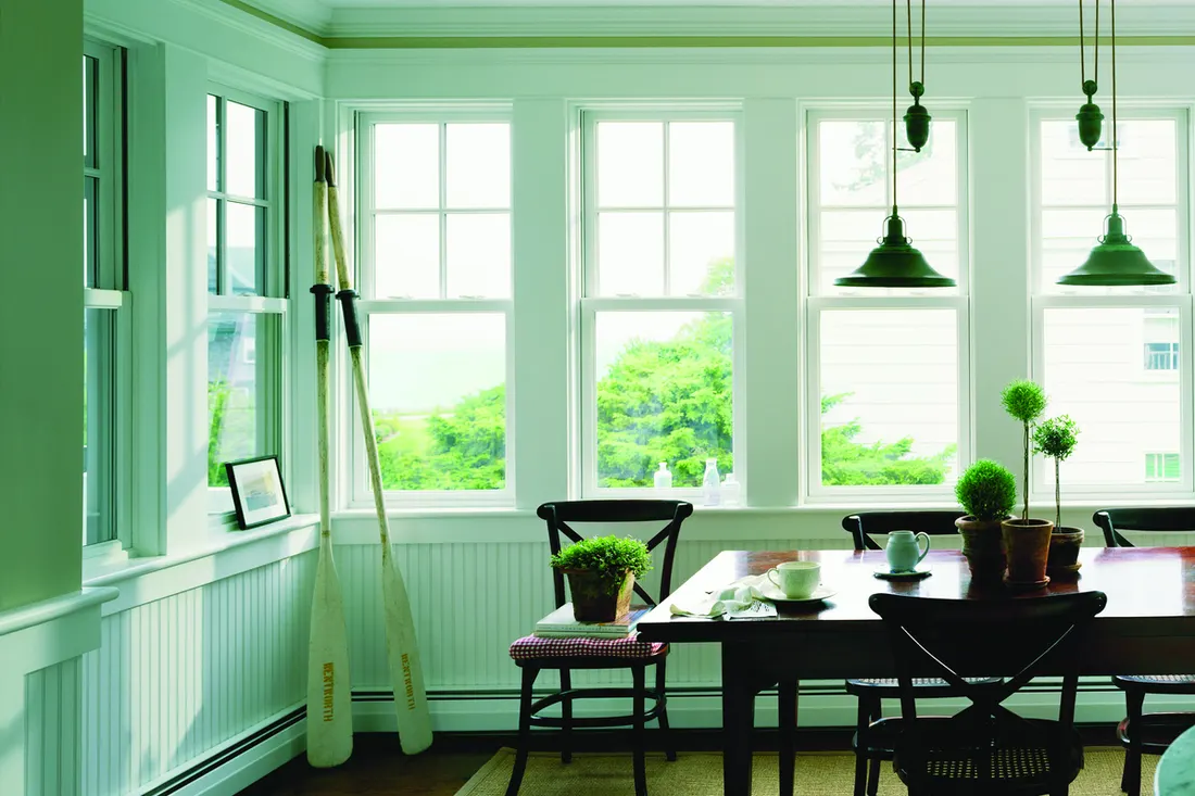 Row of white double-hung grid windows along a green dining room wall