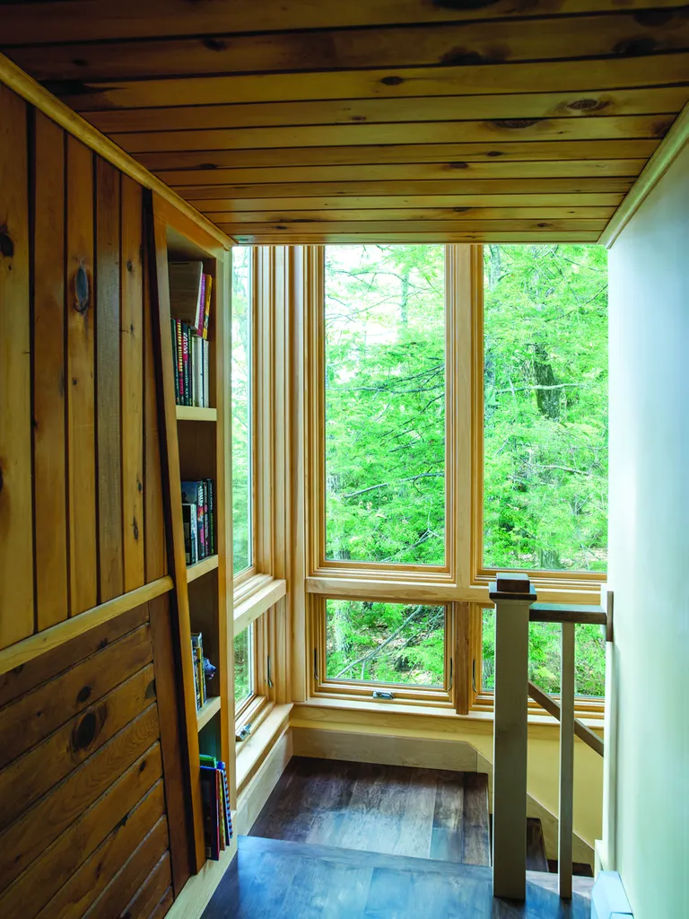 Tall natural wood windows in a pine-paneled stairwell landing overlooking a green forest