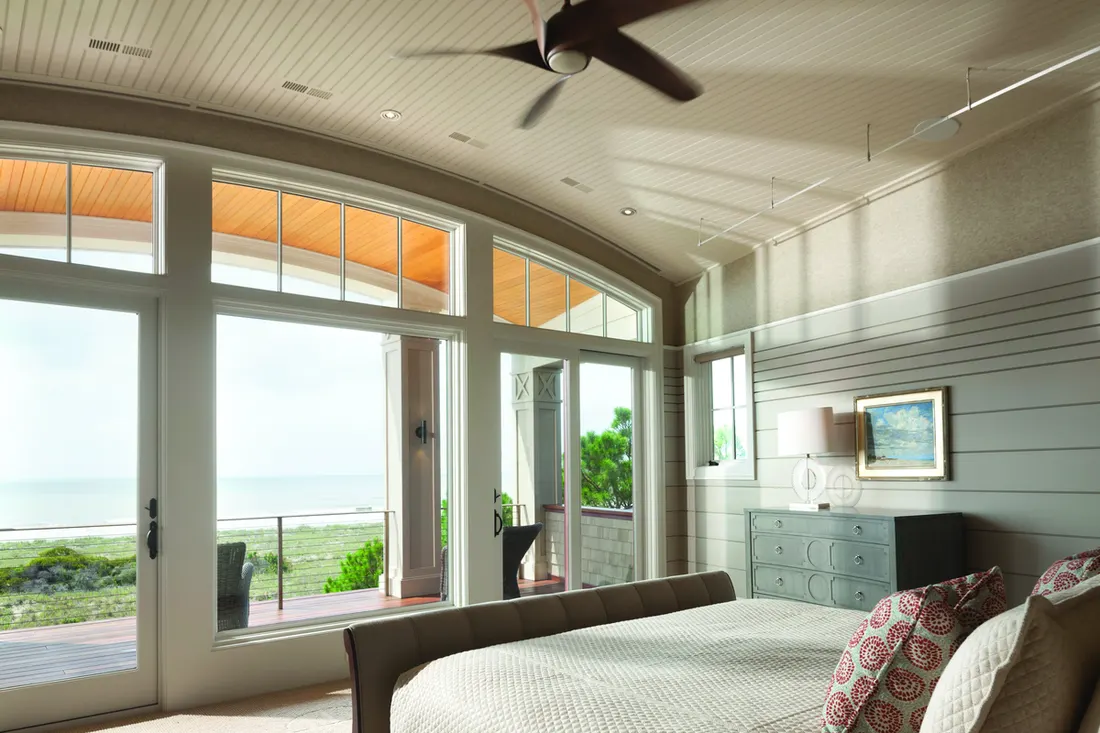 Bedroom with large white-framed picture windows and glass doors overlooking an ocean view