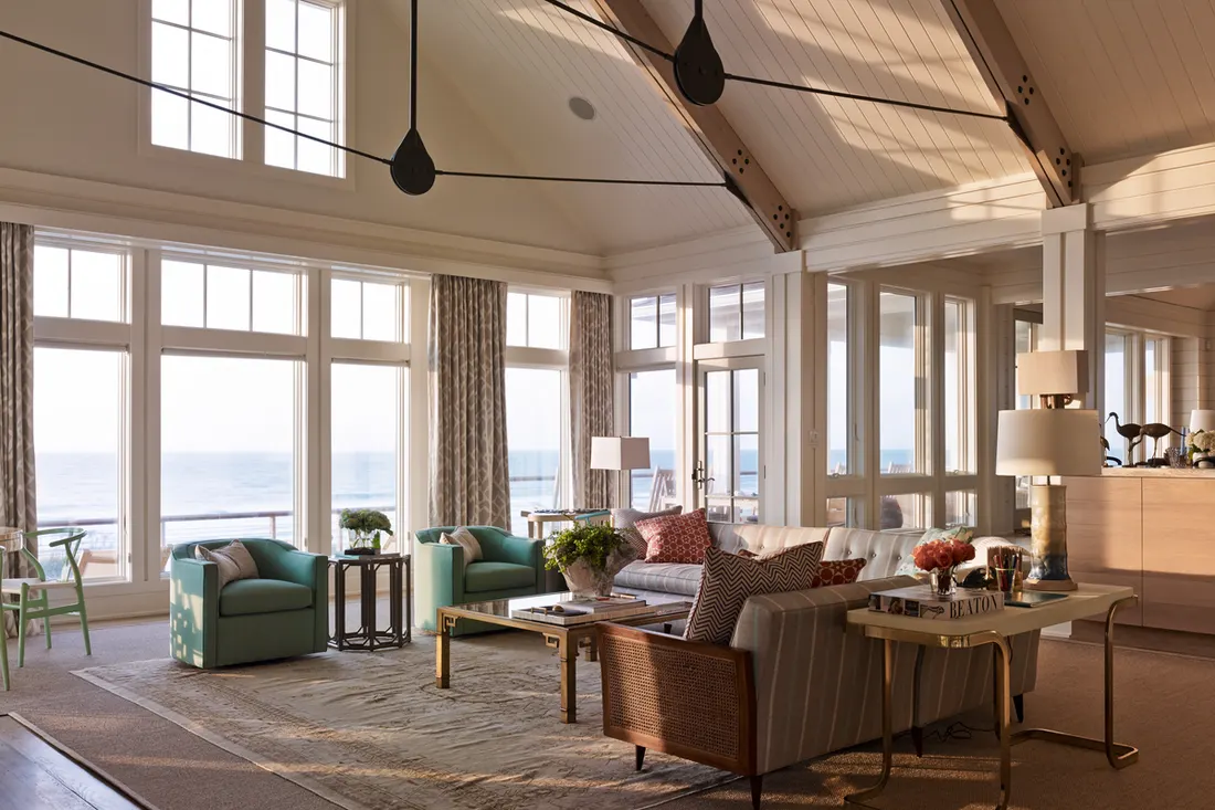 Large white-trimmed windows and glass doors overlooking the ocean in a bright living room