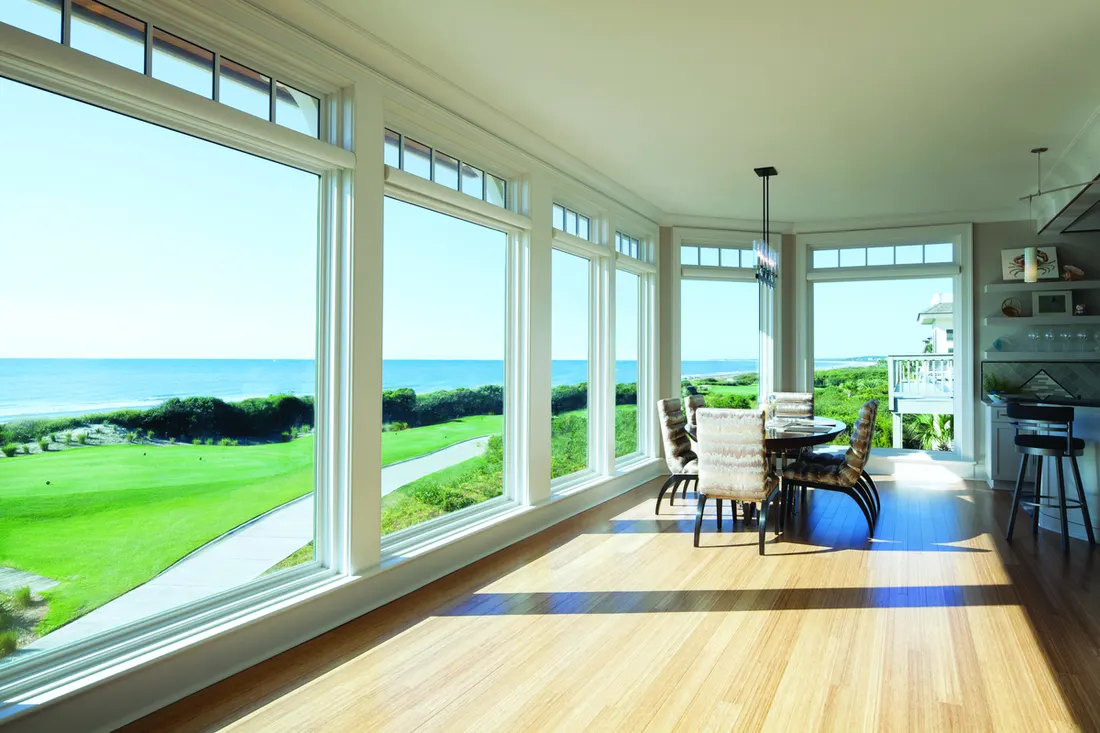 Sunlit room with wood floors and large white-framed windows overlooking the ocean and golf course