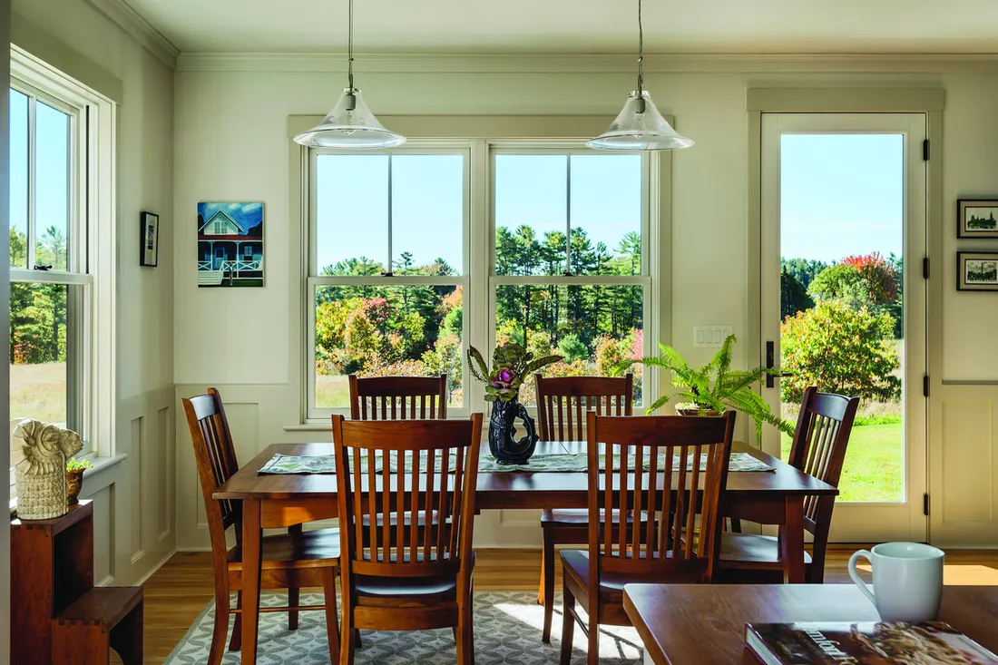 Dining room with white-trimmed double-hung windows and glass door overlooking green trees and fields