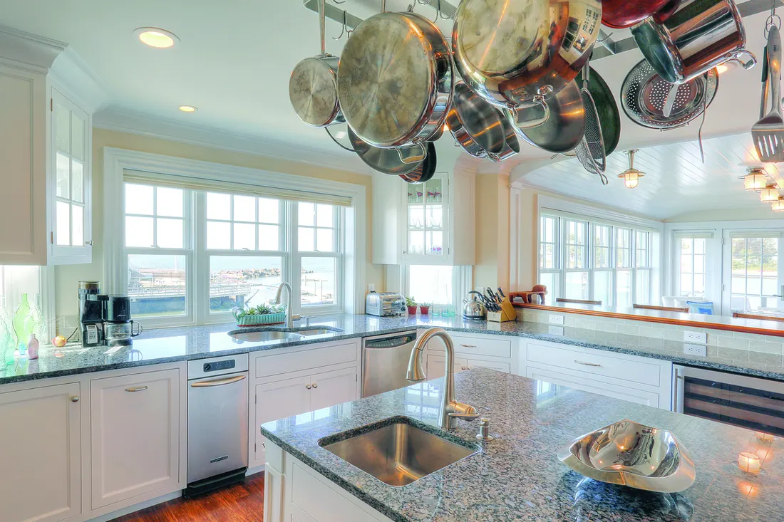 Bright coastal kitchen with white grid-paneled windows over grey granite countertops and an island sink
