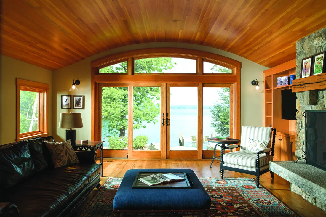 Arched wood-framed windows and glass patio doors in a rustic living room overlooking a lake