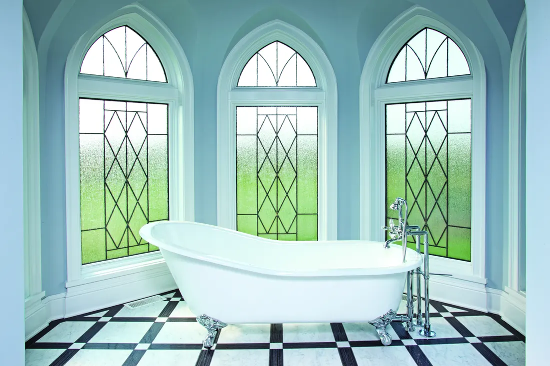 White clawfoot bathtub in front of three arched leaded glass windows with white trim