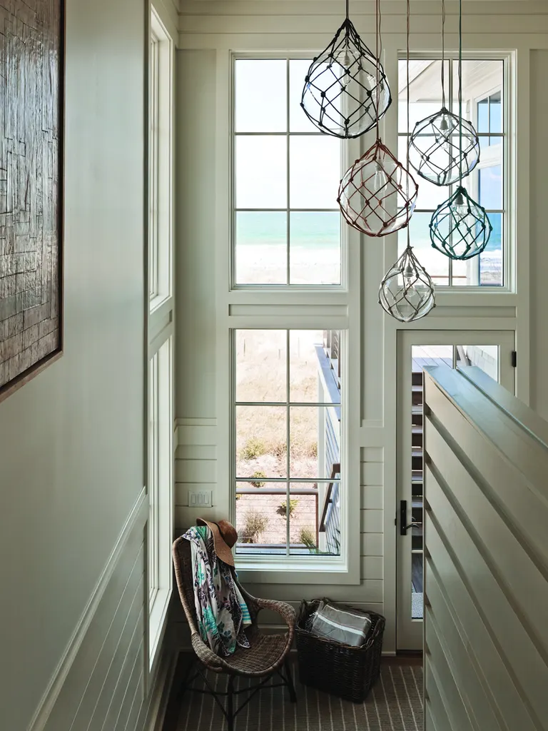 Tall white multi-pane windows offering ocean and beach views in a bright coastal stairwell
