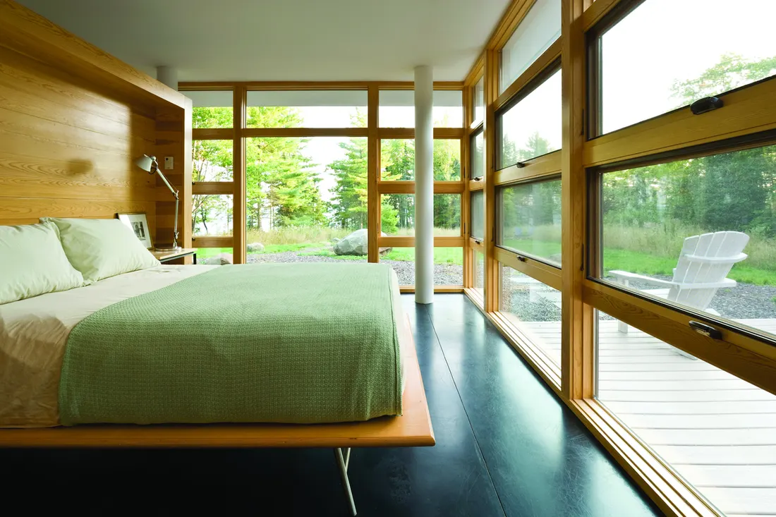Floor-to-ceiling wood-framed windows lining a modern bedroom with views of an outdoor patio