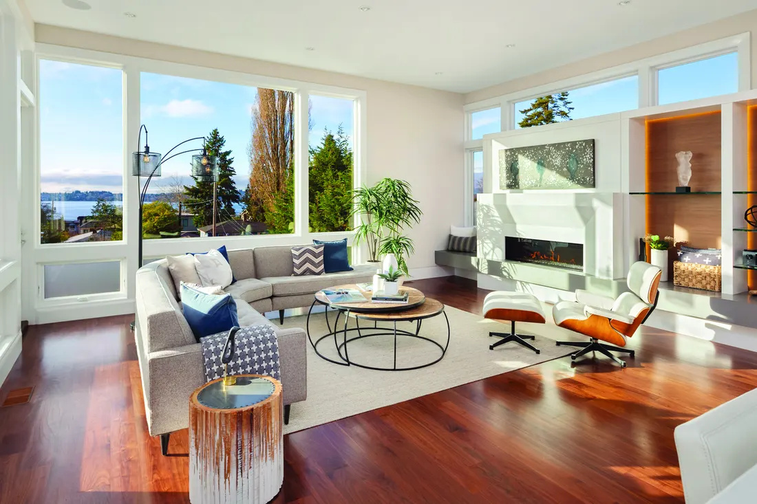 Modern living room with large white-framed picture windows overlooking trees and water