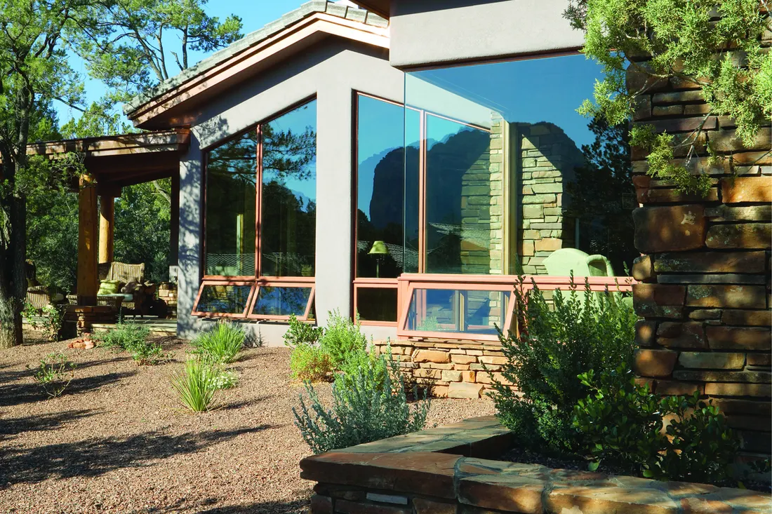 Large picture windows with open awning vents on a stone and stucco home exterior