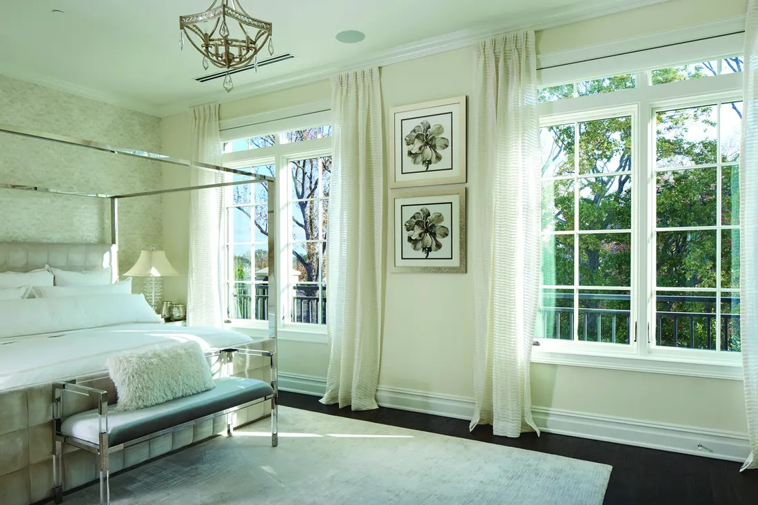 White-framed multi-pane casement windows with sheer curtains in a bright, modern bedroom overlooking outdoor trees