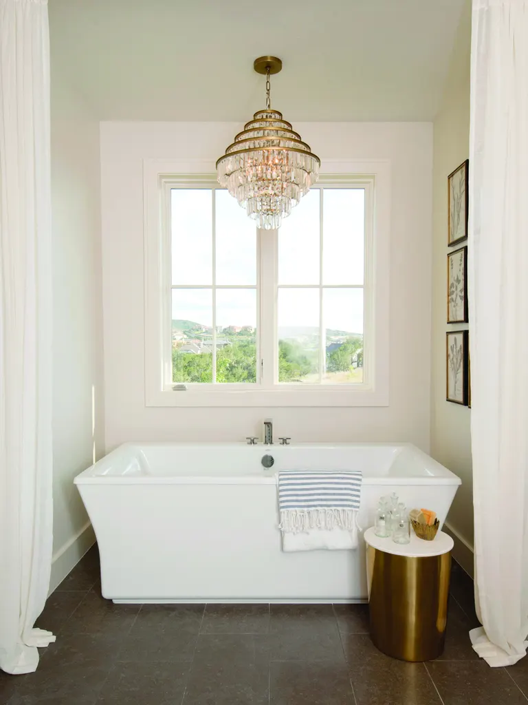 White-framed gridded window above a freestanding bathtub in a bright bathroom with chandelier