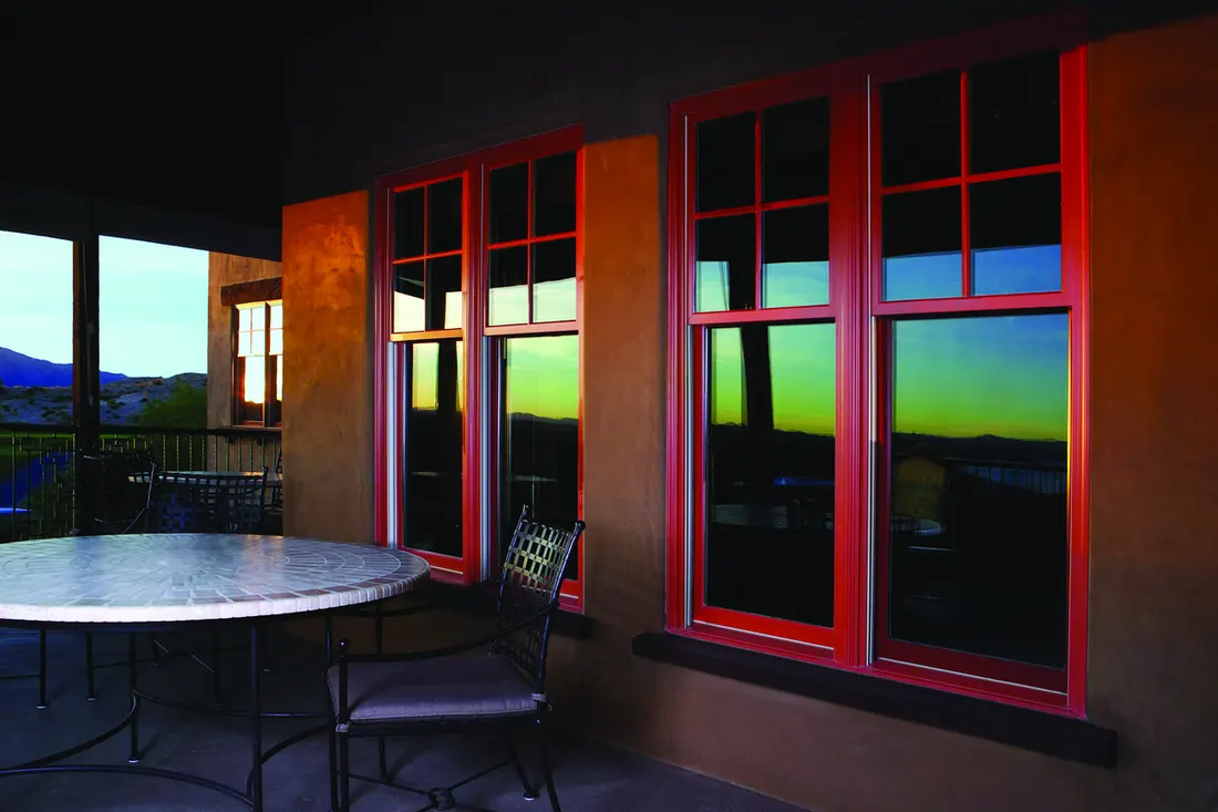 Red-framed double-hung windows set into brown stucco patio walls reflecting the outdoor landscape