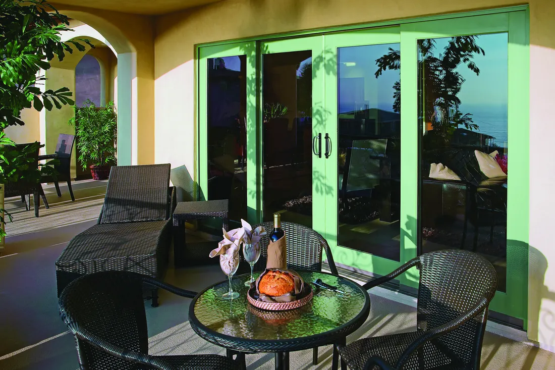 Four-panel light green sliding glass patio doors behind outdoor wicker dining and lounge furniture