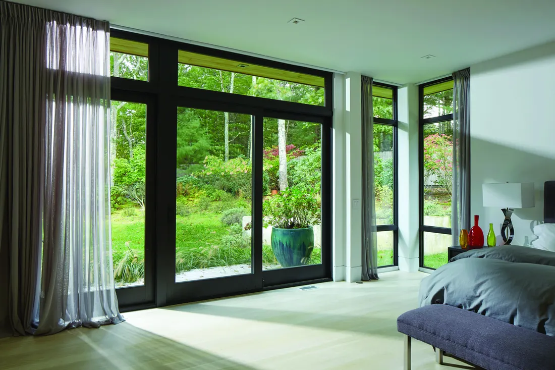 Black-framed sliding glass patio doors in a modern bedroom overlooking a lush green garden