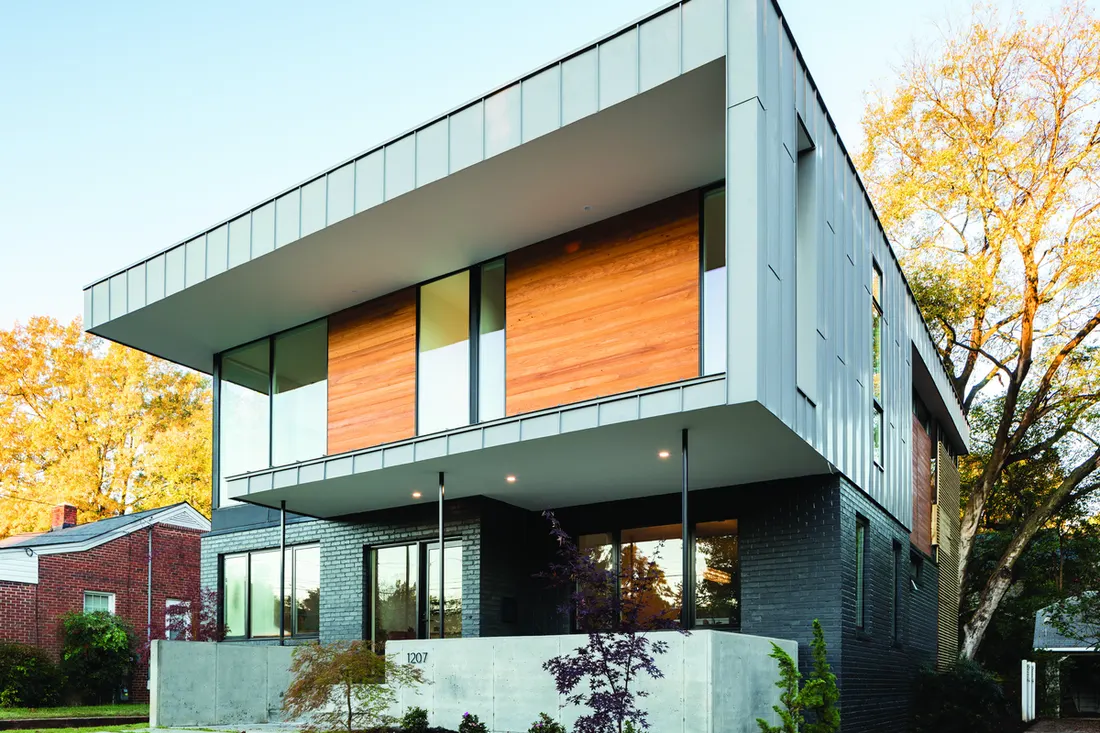 Modern two-story house with large glass windows, wood siding, and gray metal panels on a sunny day