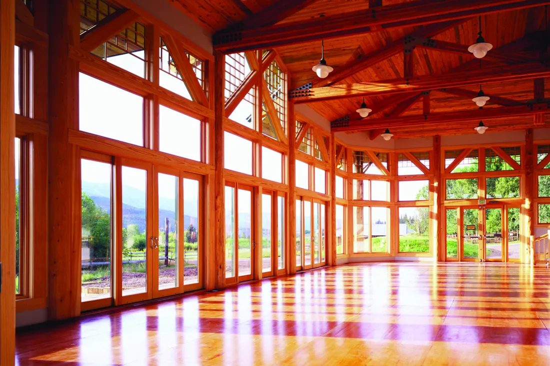 Spacious wooden hall lined with floor-to-ceiling glass windows and glass doors overlooking the outdoors