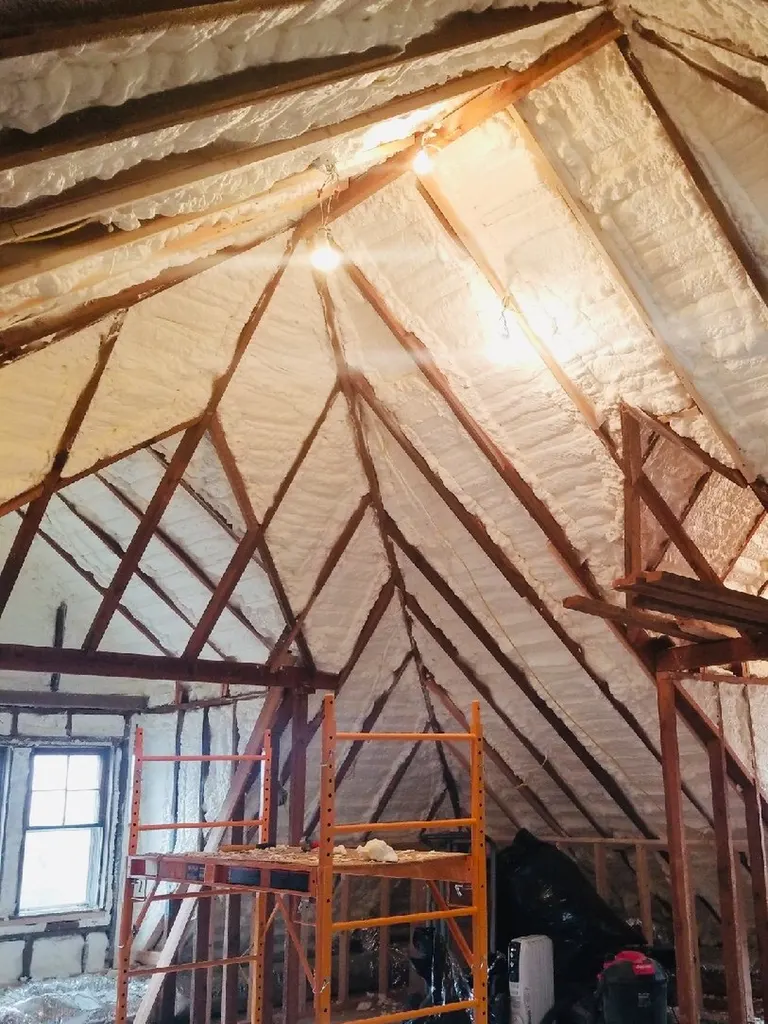 White spray foam insulation between wooden rafters in an attic with orange scaffolding
