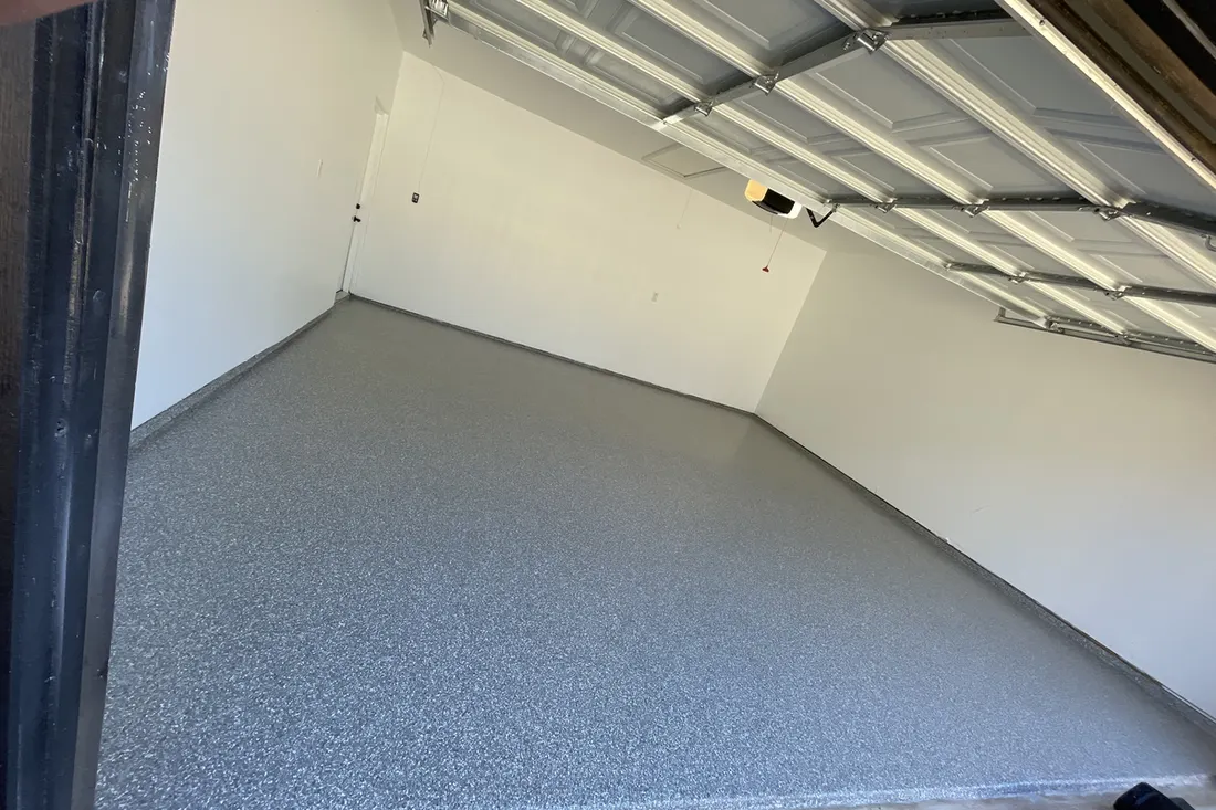 Empty garage interior featuring a gray speckled epoxy coated concrete floor and white walls