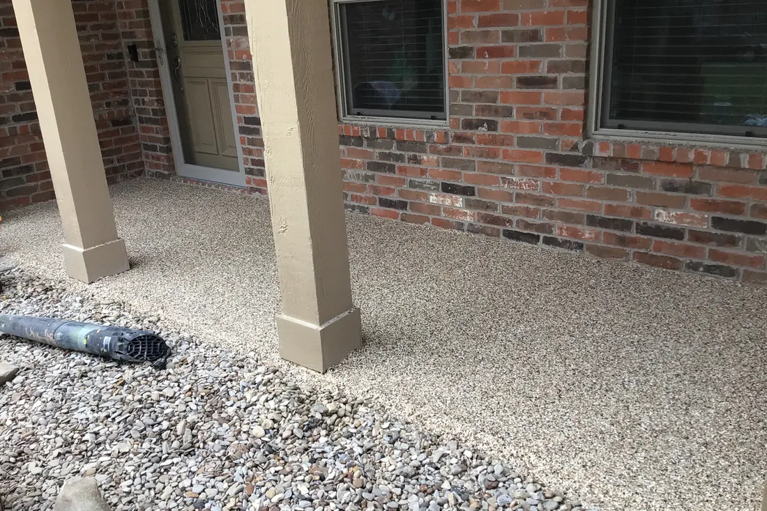 Coated beige speckled concrete porch floor along red brick exterior wall and tan pillars