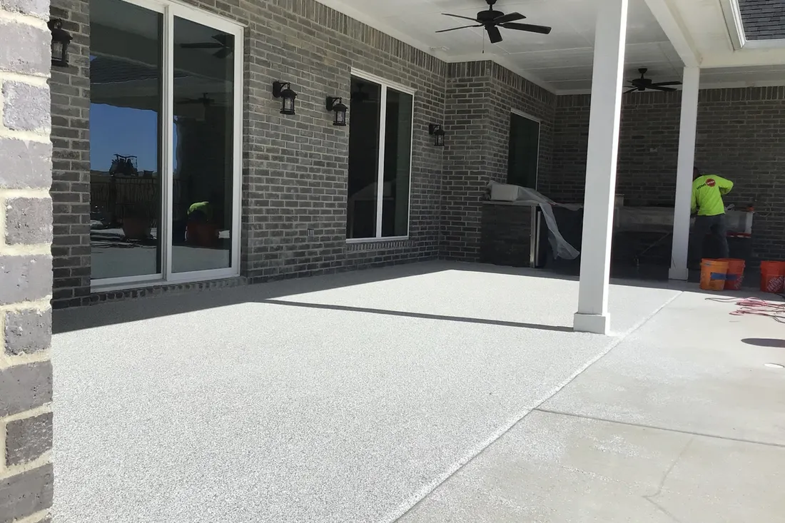 Light gray speckled concrete coating applied to a covered brick patio floor with white pillars