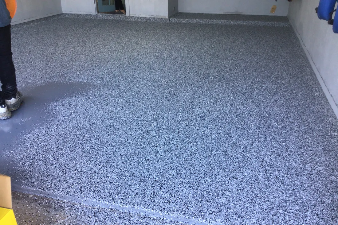 Freshly coated gray speckled flake epoxy covering an indoor garage concrete floor