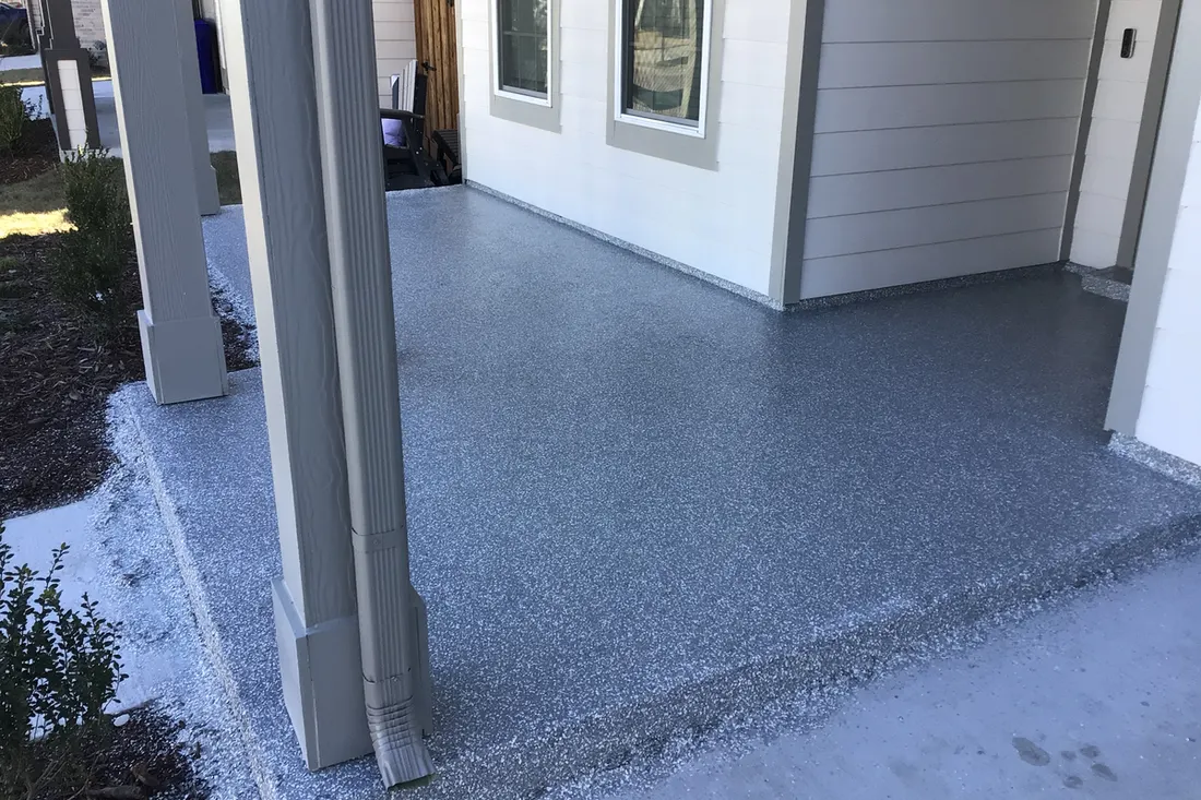 Gray speckled concrete coating on a covered house front porch with white siding