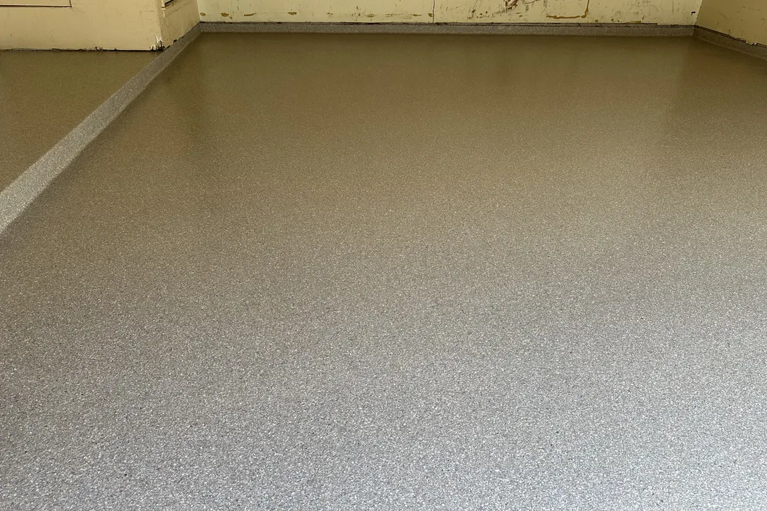 Smooth beige epoxy coated concrete floor with subtle speckled texture in an interior garage space