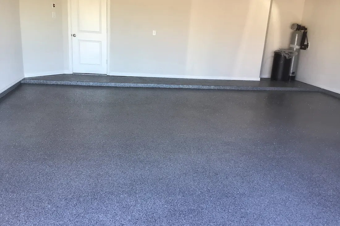 Empty garage interior with a gray speckled epoxy coated concrete floor and white walls
